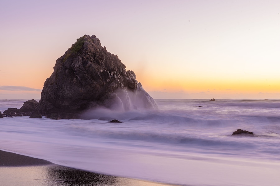 Un afloramiento rocoso con olas rompiendo al atardecer.