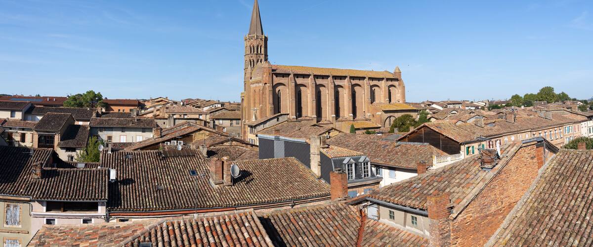 A historic church with a tall spire, surrounded by traditional European buildings with tiled roofs.