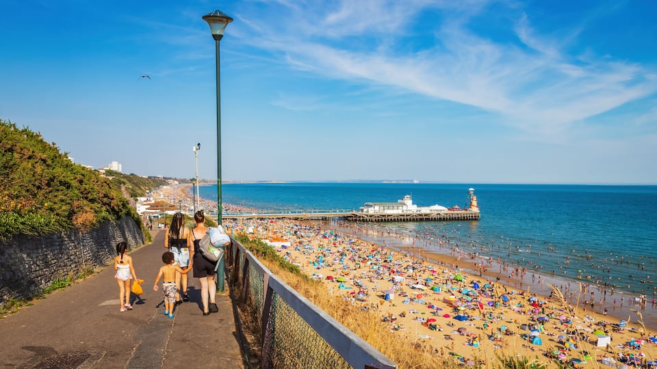 A coastal promenade with a beach, a pier, and a lighthouse.