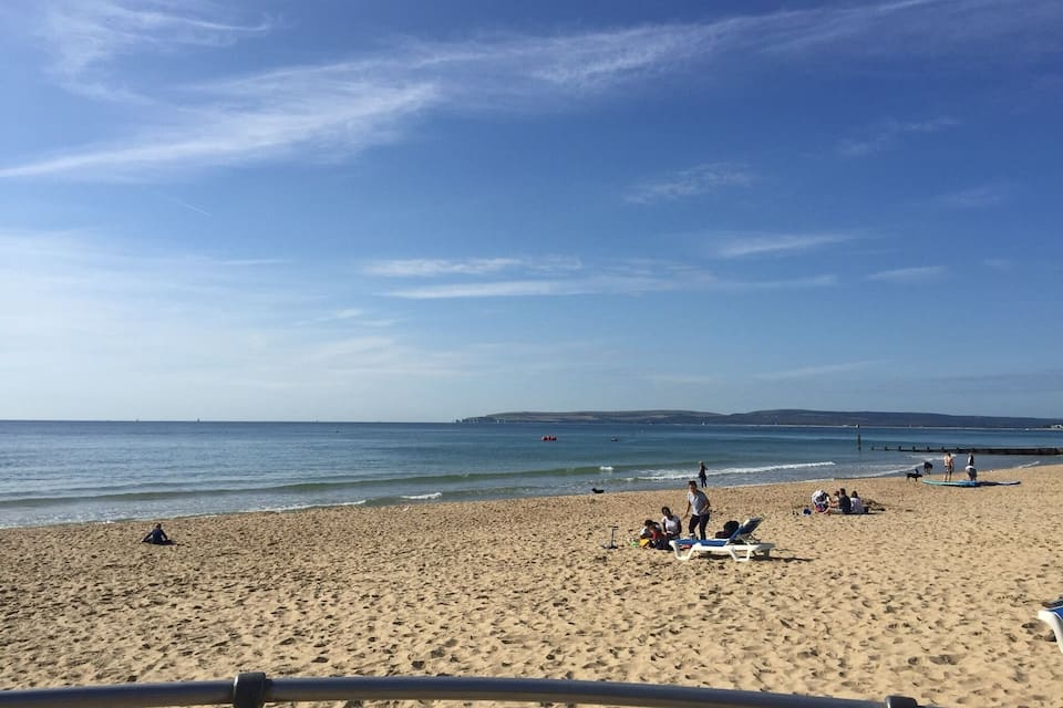 A sandy beach with people sunbathing and swimming.