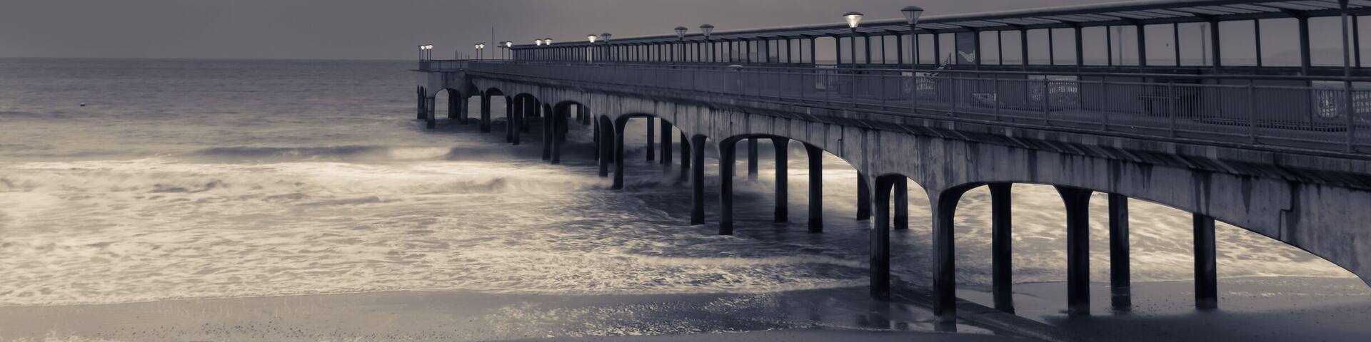 A pier extending into the ocean with a cloudy sky above.