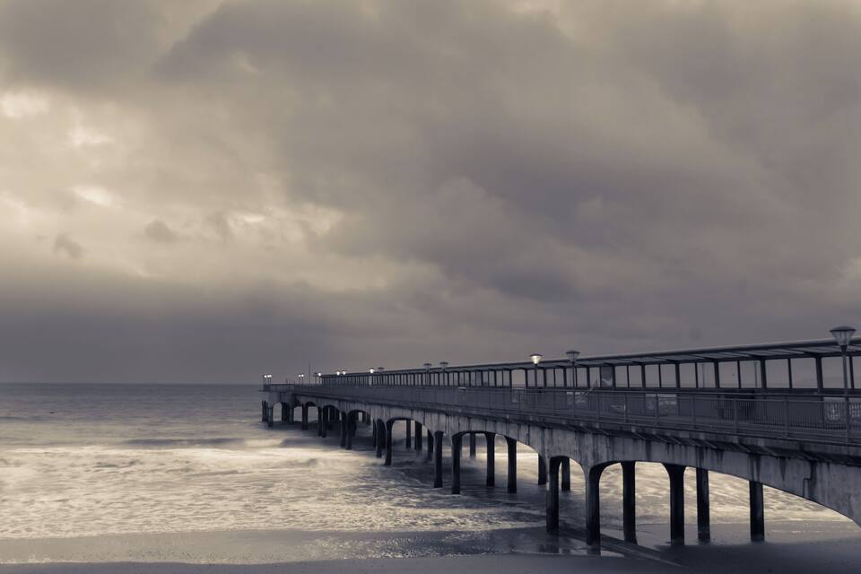 A pier extending into the ocean with a cloudy sky above.