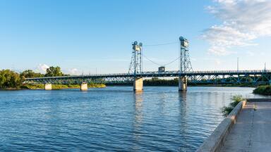 A blue metal bridge over a calm river with greenery on the banks.