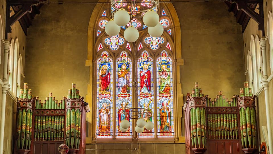 A stained glass window with religious figures, a wooden organ, and a vaulted ceiling.