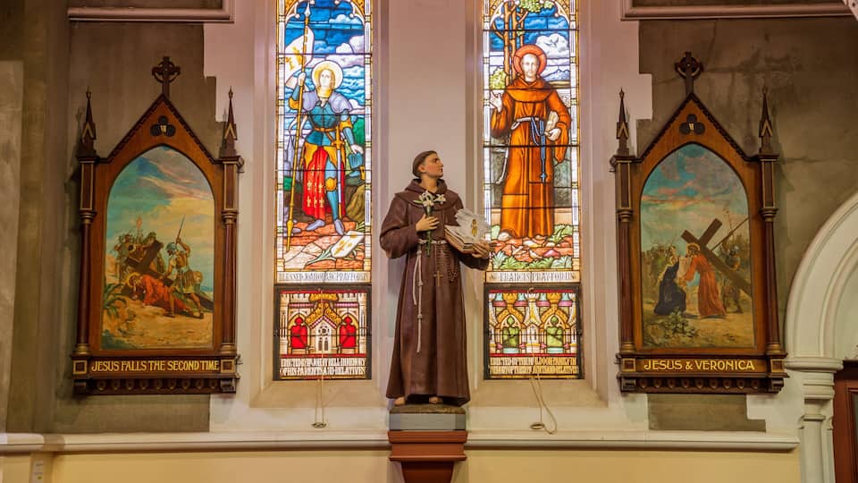 Una finestra a vetri colorati con figure religiose, un pulpito in legno e un dipinto di Gesù e Veronica.