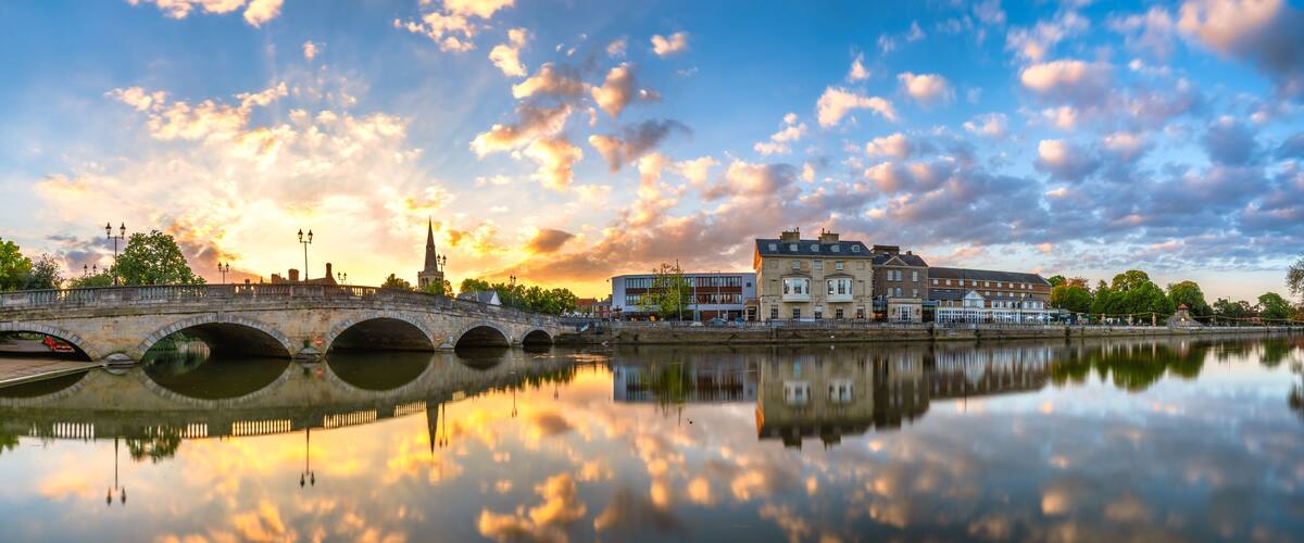 A river with a stone bridge, a church spire, and buildings reflecting in the water.