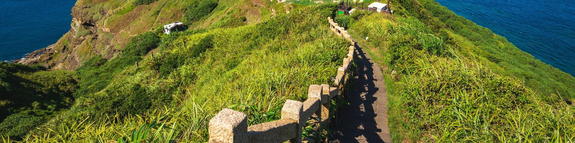 A coastal landscape with a lighthouse on a hill, a winding path, and the ocean in the background.