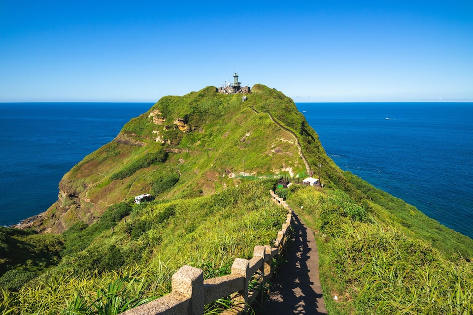 A coastal landscape with a lighthouse on a hill, a winding path, and the ocean in the background.