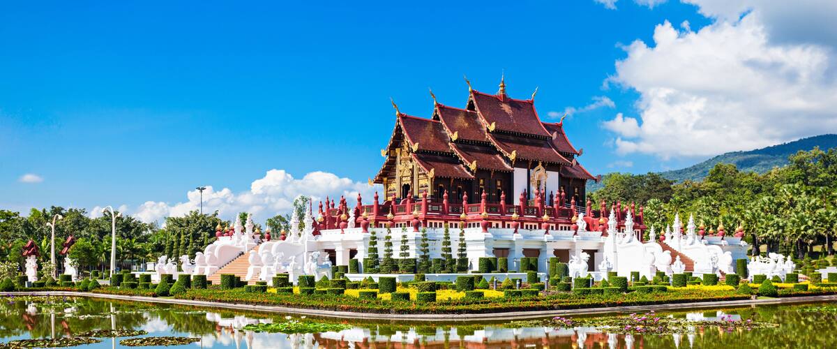 A traditional temple with a reflection in the water, surrounded by well-maintained gardens and a clear blue sky.