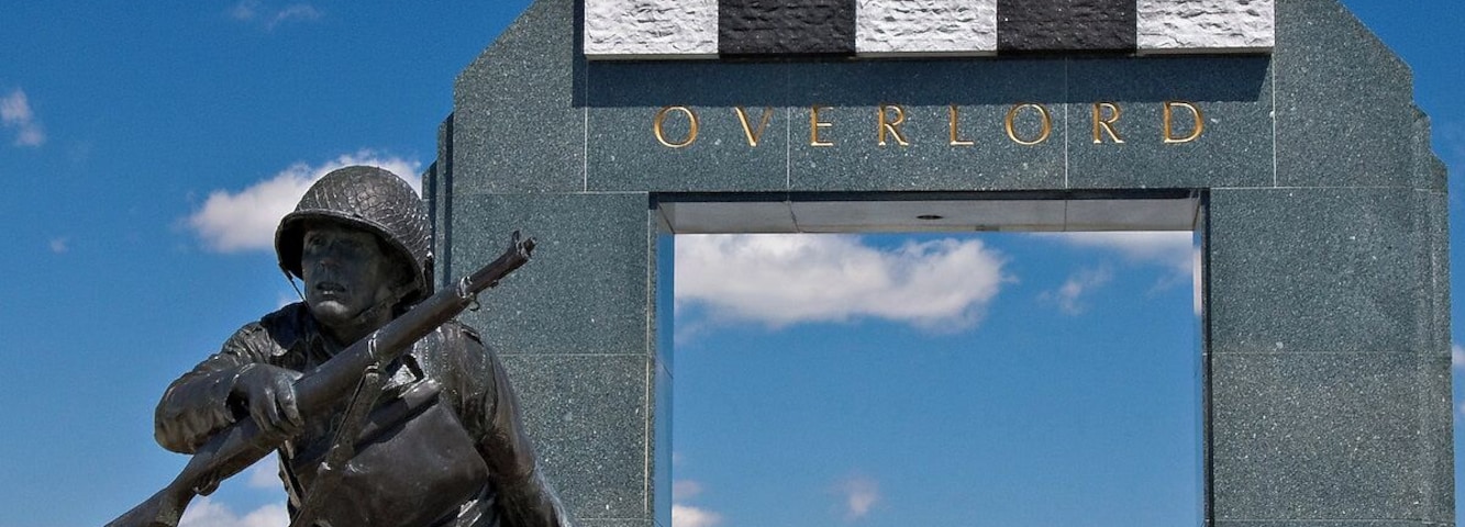 The National D-Day Memorial is an awe-inspiring tribute to the D-Day Invasion, the largest amphibious military landing the world has ever seen. Bedford, Virginia, was chosen as the location of the memorial because the community of Bedford suffered the highest per-capita D-Day losses in the nation.
The memorial is spread over 88 acres and is divided into patterns which represent the various stages or aspects of the invasion.
The centerpiece of the memorial is the Victory Plaza arch, which can be seen for miles. The arch contains a single word, Overlord, referring to Operation Overlord, the code name of the Battle of Normandy. The arch is crowned with five chiseled elements designed to resemble the roofs of houses seen by airborne troops as they passed over the Normandy countryside on the eve of D-Day. The chiseled elements are painted in a black and white pattern, just like the stripes painted on the wings of Allied aircraft.
