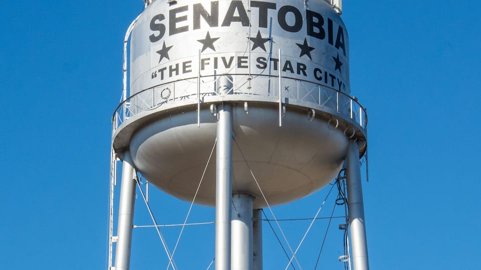 A water tower with the text "SENATOBIA THE FIVE STAR CITY" against a clear blue sky.