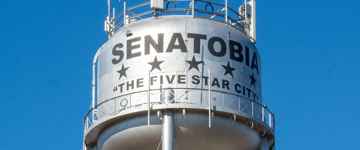 A water tower with the text "SENATOBIA THE FIVE STAR CITY" against a clear blue sky.