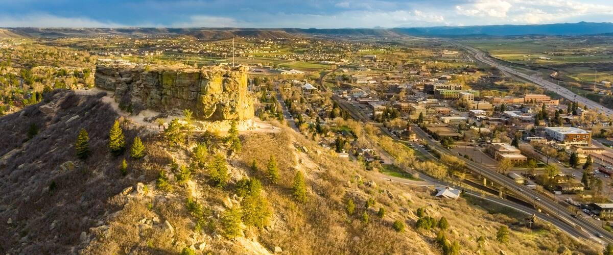 Un paysage montagneux avec une ville nichée au pied des montagnes, une autoroute et un ciel dégagé.