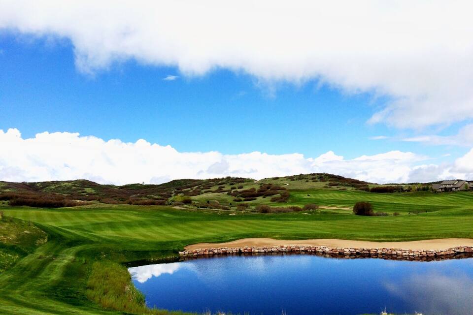 A golf course with a pond and rolling hills.