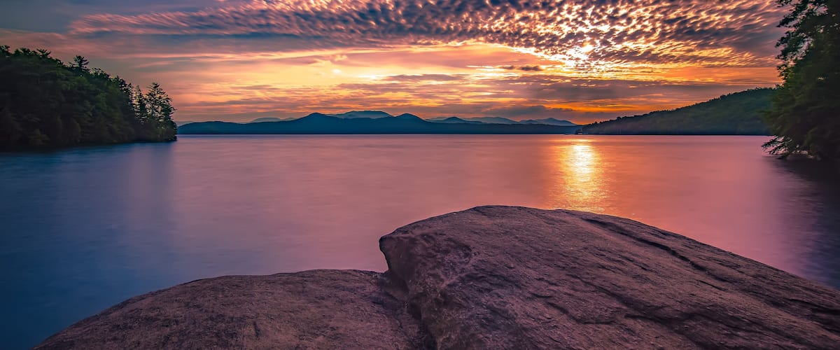 Een rustig meer met bergen op de achtergrond en een zonsondergang.