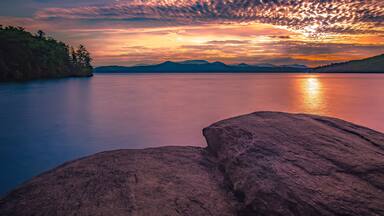 A calm lake with mountains in the background and a sunset.