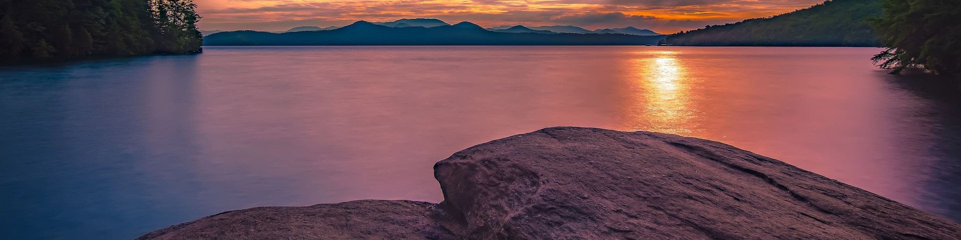 Um lago tranquilo com montanhas ao fundo e um pôr do sol.