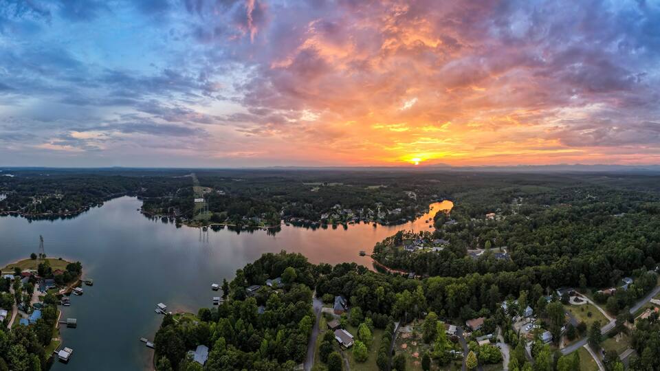 A sunset over a lake surrounded by dense forests and residential areas.