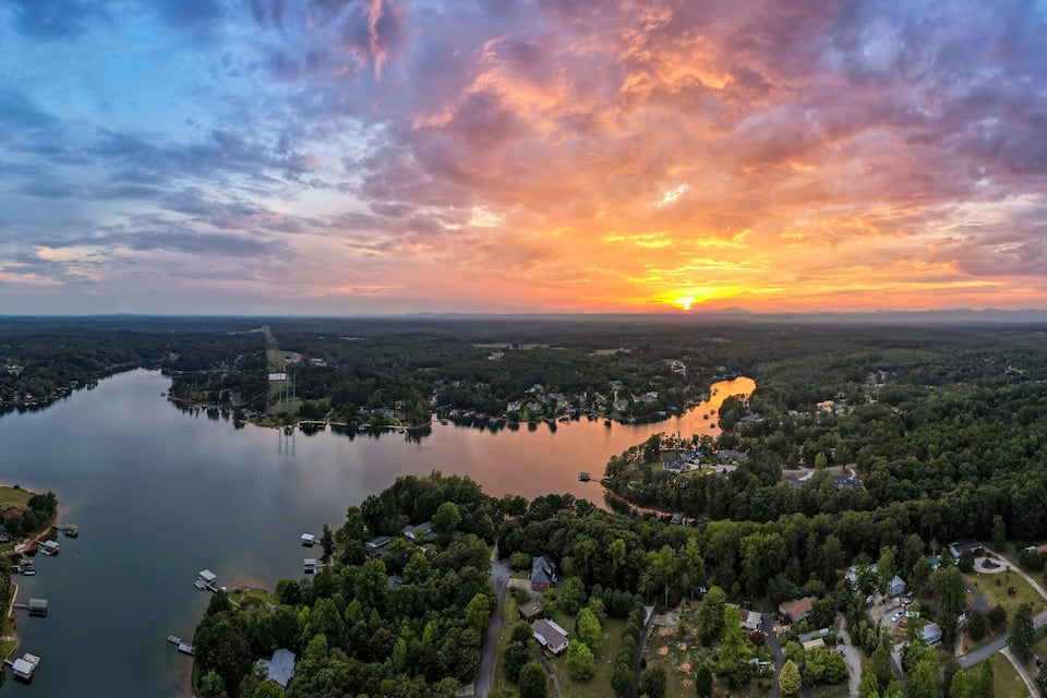 A sunset over a lake surrounded by dense forests and residential areas.