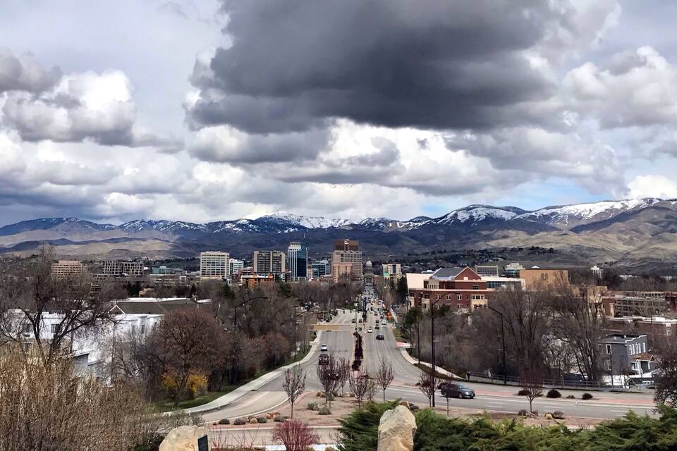 A cityscape with a mountain range in the background under a cloudy sky.