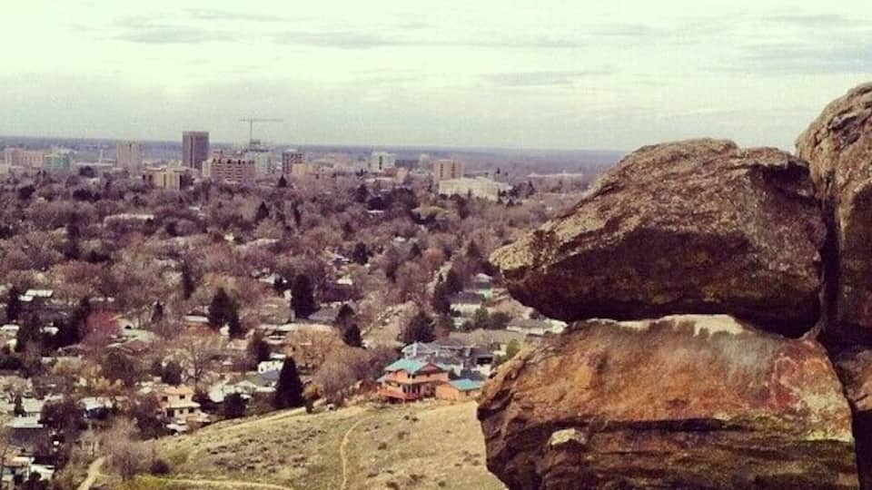A rocky outcrop overlooking a cityscape with buildings and sparse vegetation.