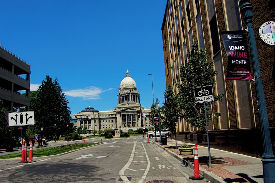 A city street with a large government building, a bike lane sign, and a banner for Idaho Wine Month.