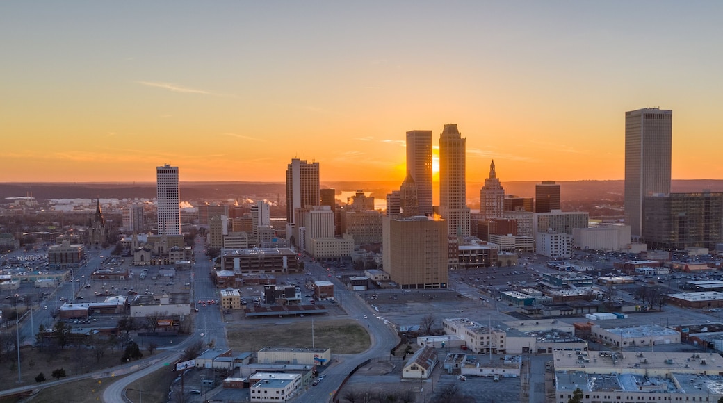 A cityscape with a prominent building with a spire, several high-rise buildings, and a sunset in the background.