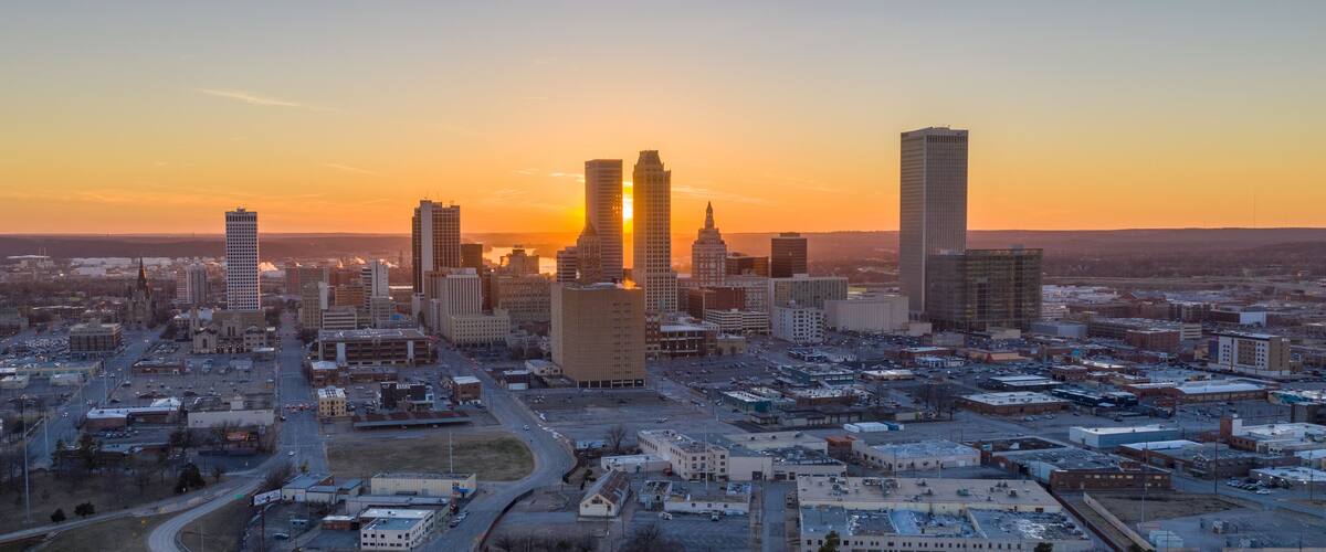 A cityscape with a prominent building with a spire, several high-rise buildings, and a sunset in the background.