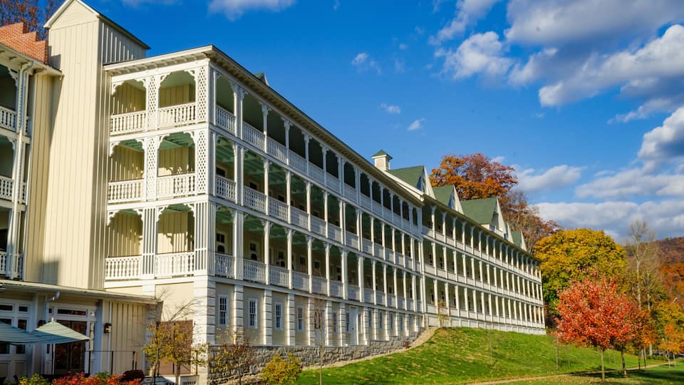 A large, white, multi-story building with a symmetrical facade, arched windows, and a green roof.