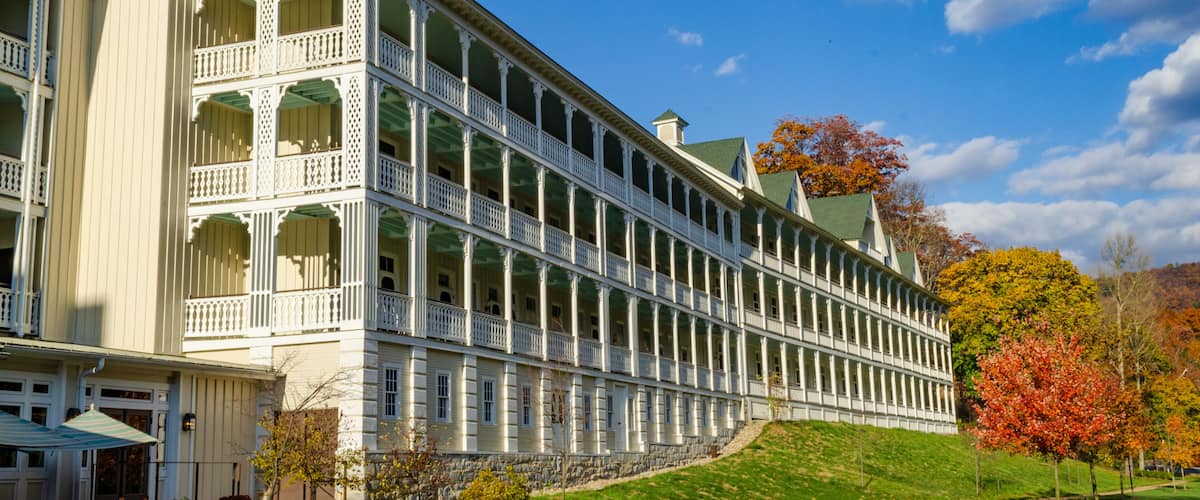 A large, white, multi-story building with a symmetrical facade, arched windows, and a green roof.