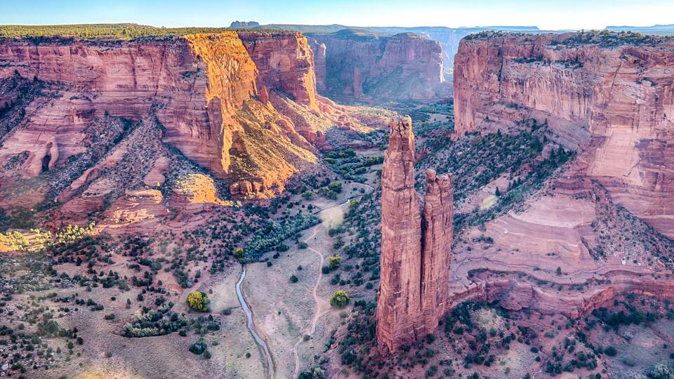 A canyon with red rock formations, a river, and sparse vegetation.