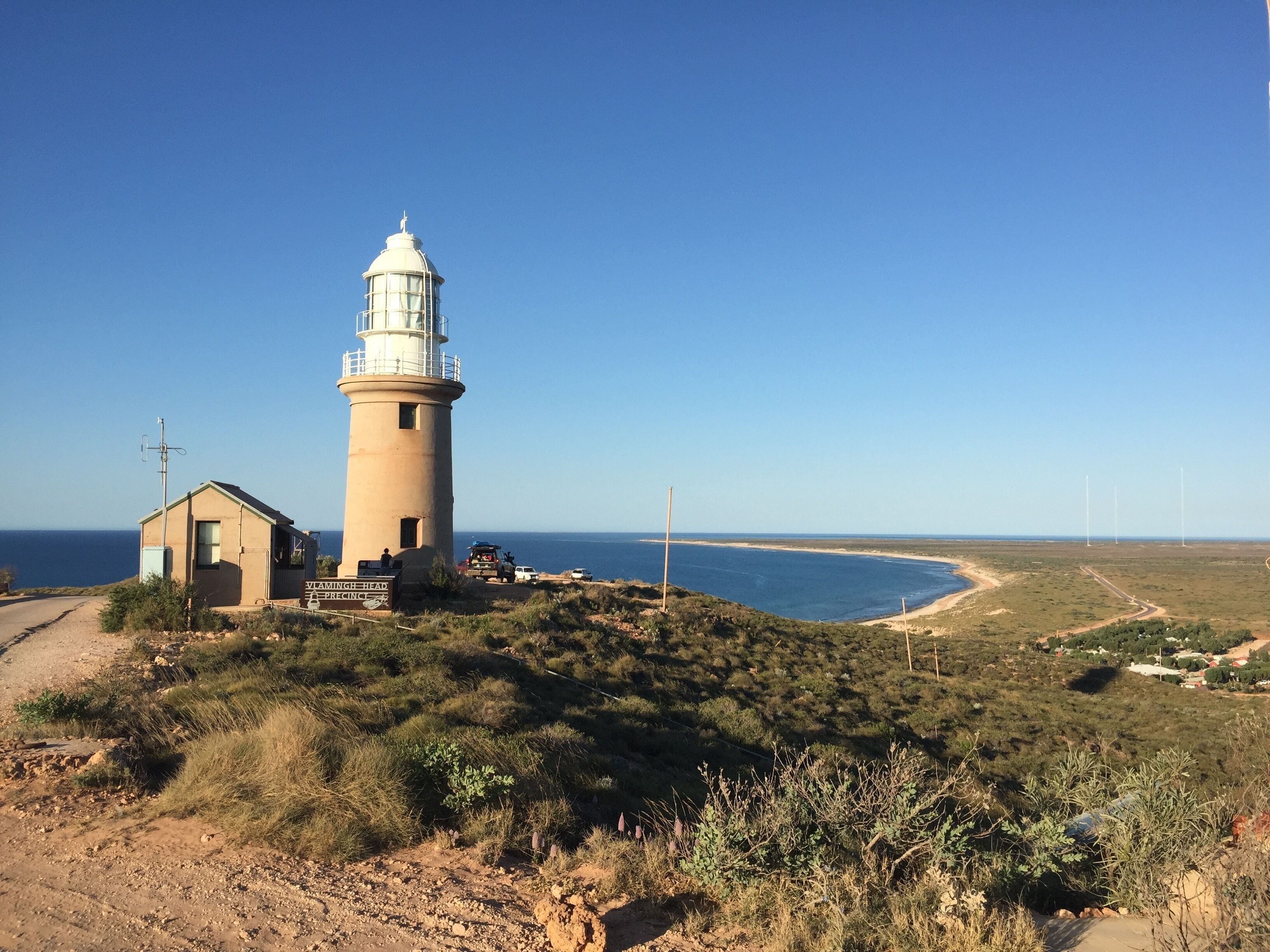 A lighthouse, a small building, and a coastal landscape with a clear sky.