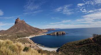 Eine Küstenlandschaft mit einem markanten Felsen, einem Sandstrand und einem klaren blauen Meer.
