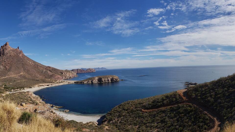 A coastal landscape with a prominent rocky peak, a sandy beach, and a clear blue sea.