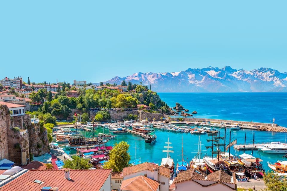 A coastal town with a marina, historic buildings, and a mountain range in the background.
