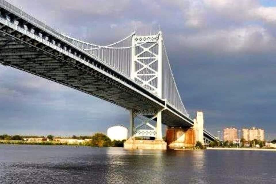A suspension bridge over a river with a cityscape in the background.