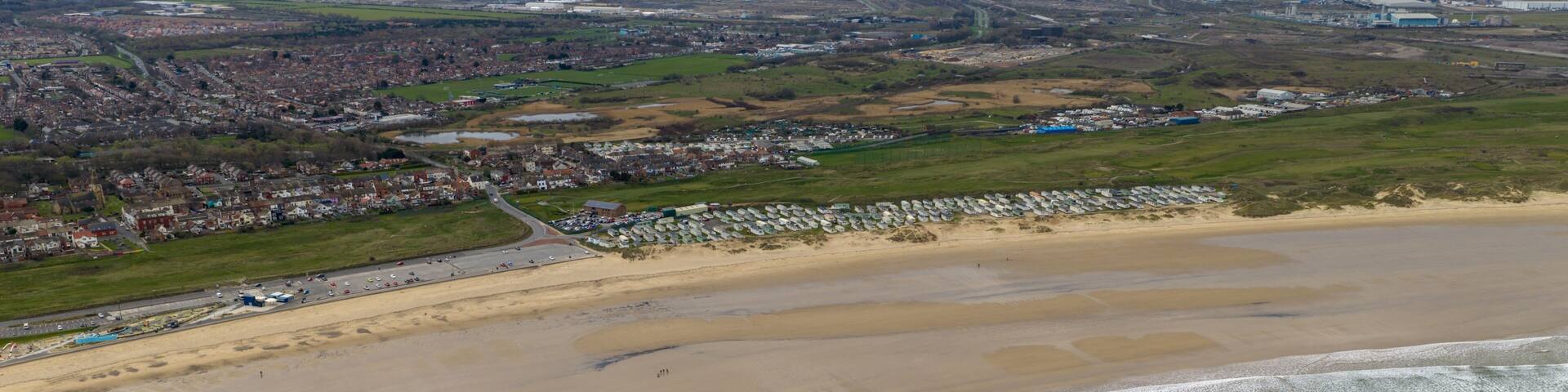 Aerial view of the Redcar in Middlesbrough UK coastline showing sandy beach waves caravan park and nearby residential area with wide open shoreline and coastal environment in the spring time