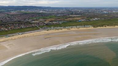 Aerial view of the Redcar in Middlesbrough UK coastline showing sandy beach waves caravan park and nearby residential area with wide open shoreline and coastal environment in the spring time