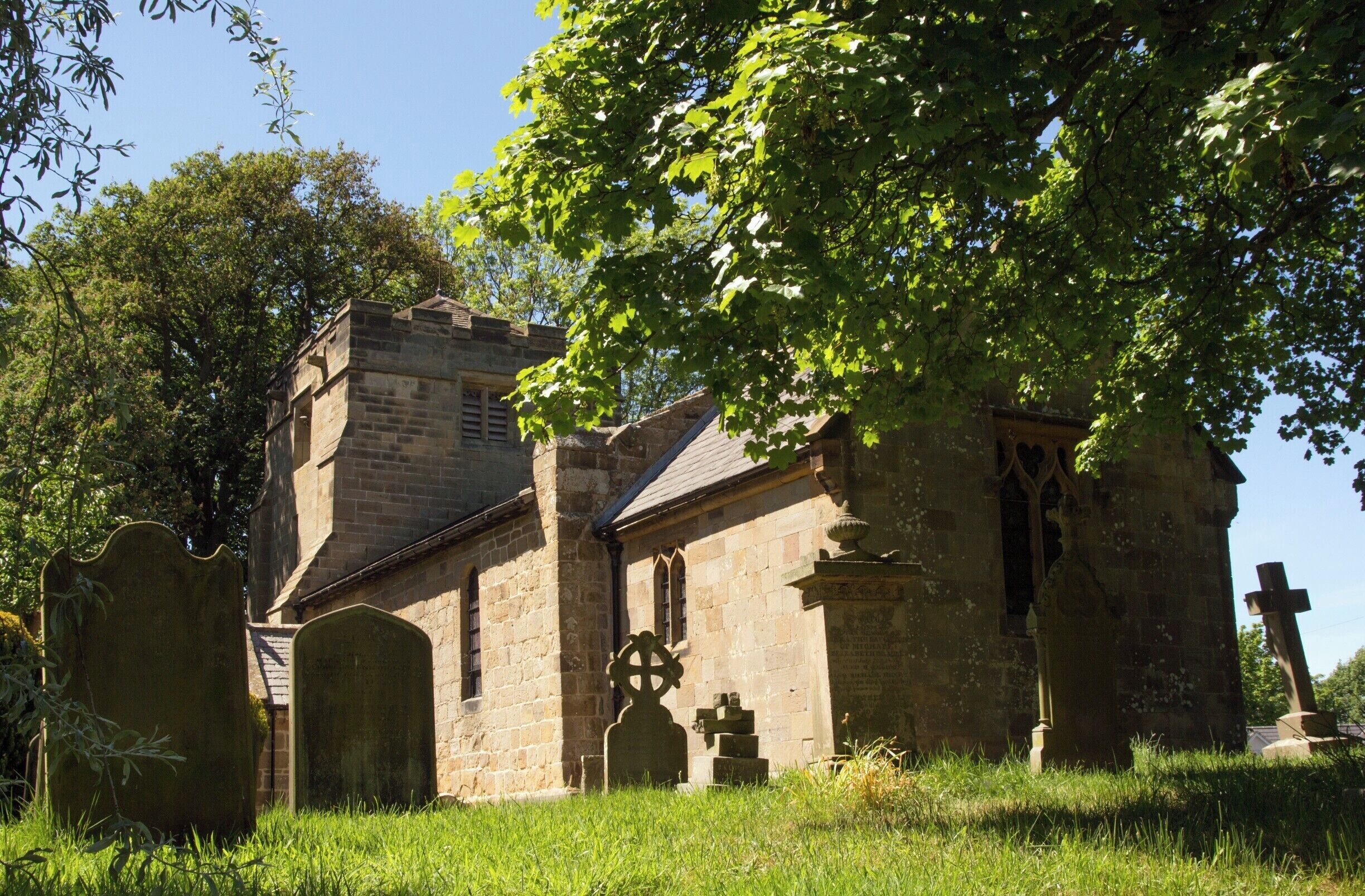 A stone church with a bell tower and a large tree in front.