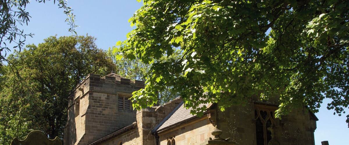A stone church with a bell tower and a large tree in front.