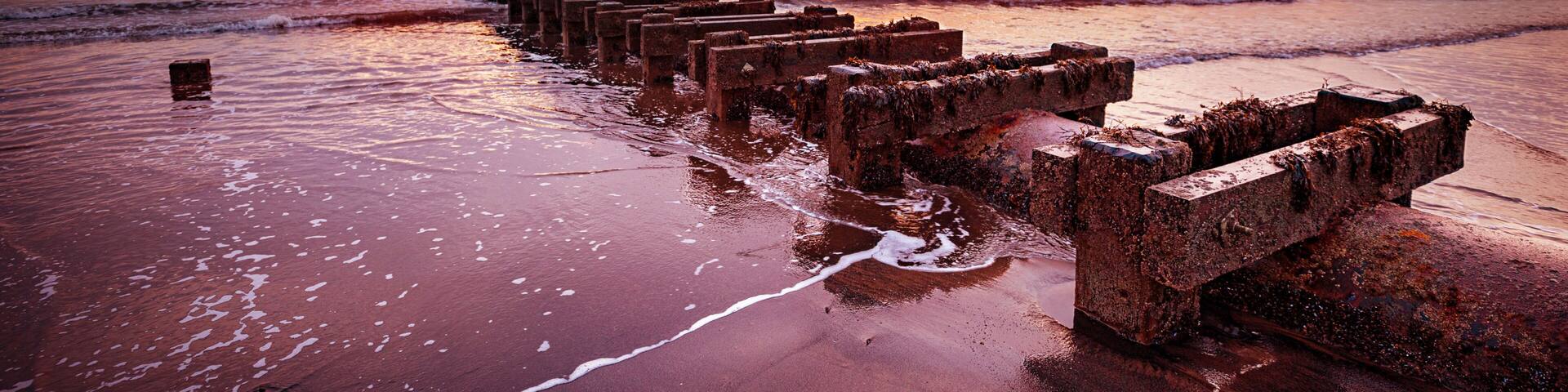 A sunset over a beach with a rusted pier extending into the water.