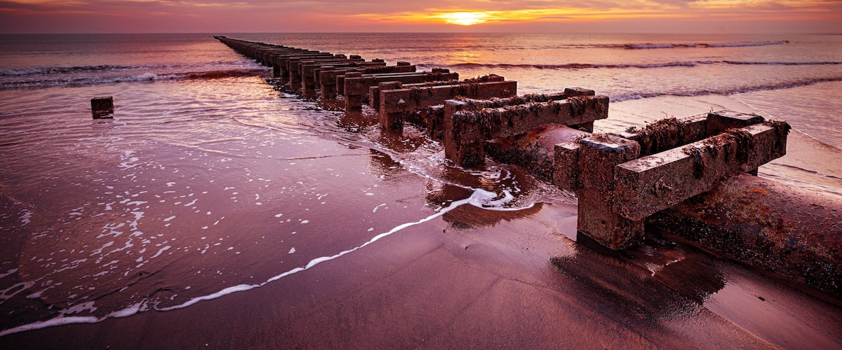 A sunset over a beach with a rusted pier extending into the water.