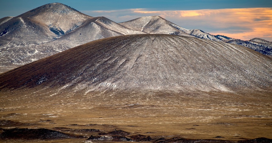 A mountainous landscape with a prominent peak in the foreground and snow-capped mountains in the background.