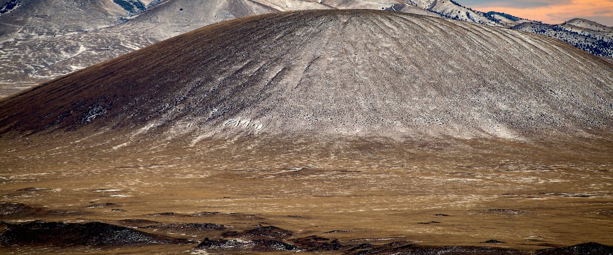 A mountainous landscape with a prominent peak in the foreground and snow-capped mountains in the background.