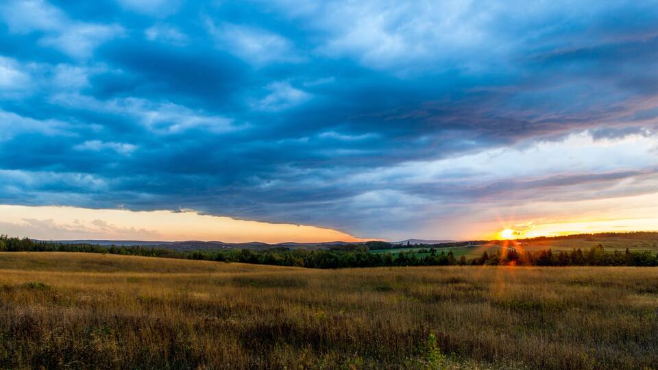 A sunset over a grassy field with a cloudy sky.