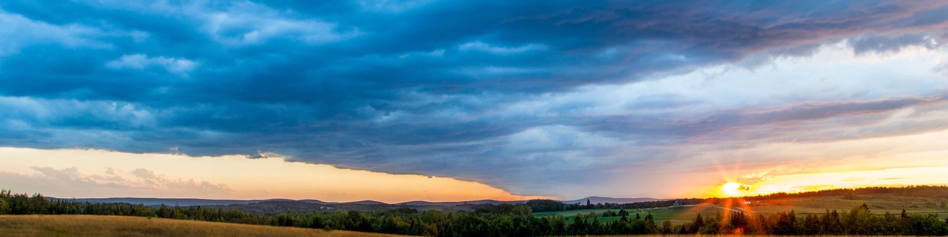 A sunset over a grassy field with a cloudy sky.