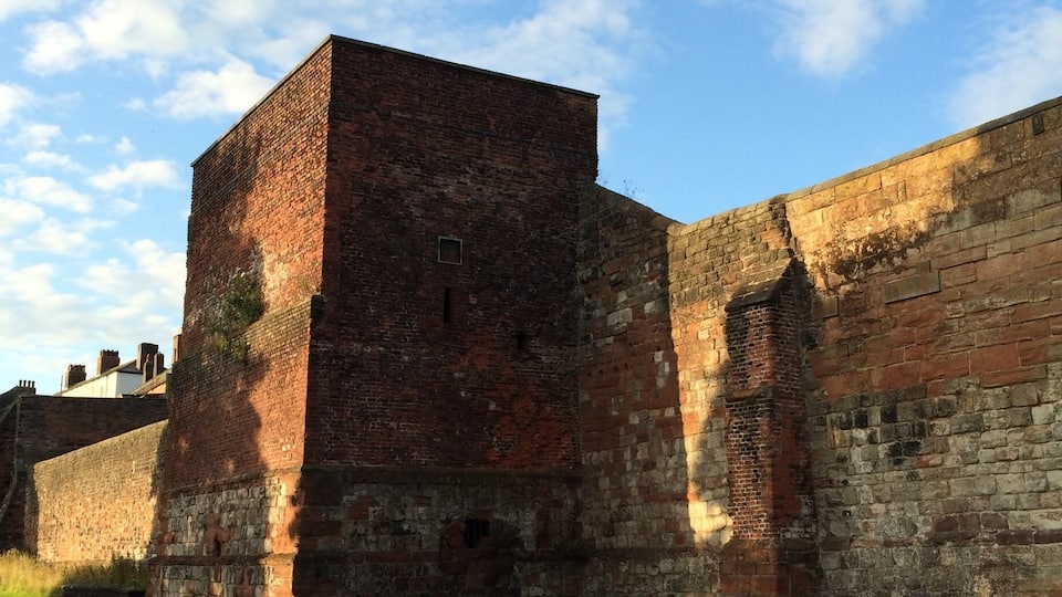 A historic brick building with a large tower, surrounded by a grassy area and a paved road.