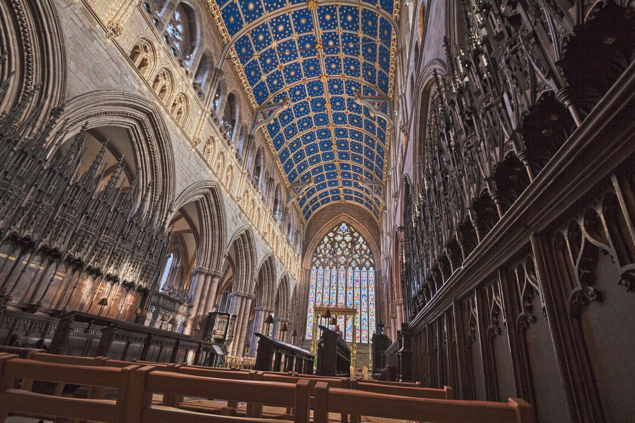 A cathedral interior with a starry blue ceiling, Gothic arches, and stained glass windows.