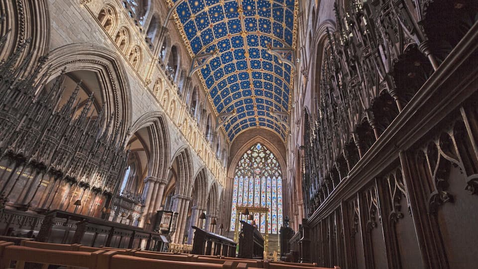 A cathedral interior with a starry blue ceiling, Gothic arches, and stained glass windows.