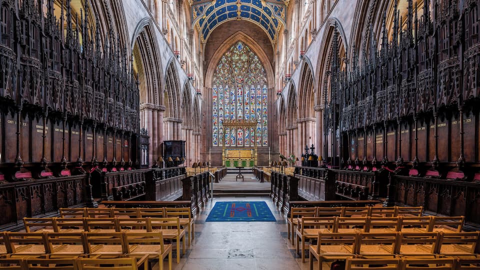 An interior of a cathedral with a blue starry ceiling, wooden pews, and stained glass windows.